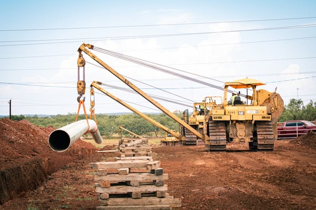 Sideboom lowering coated pipe into the trench on an onshore pipeline right-of-way