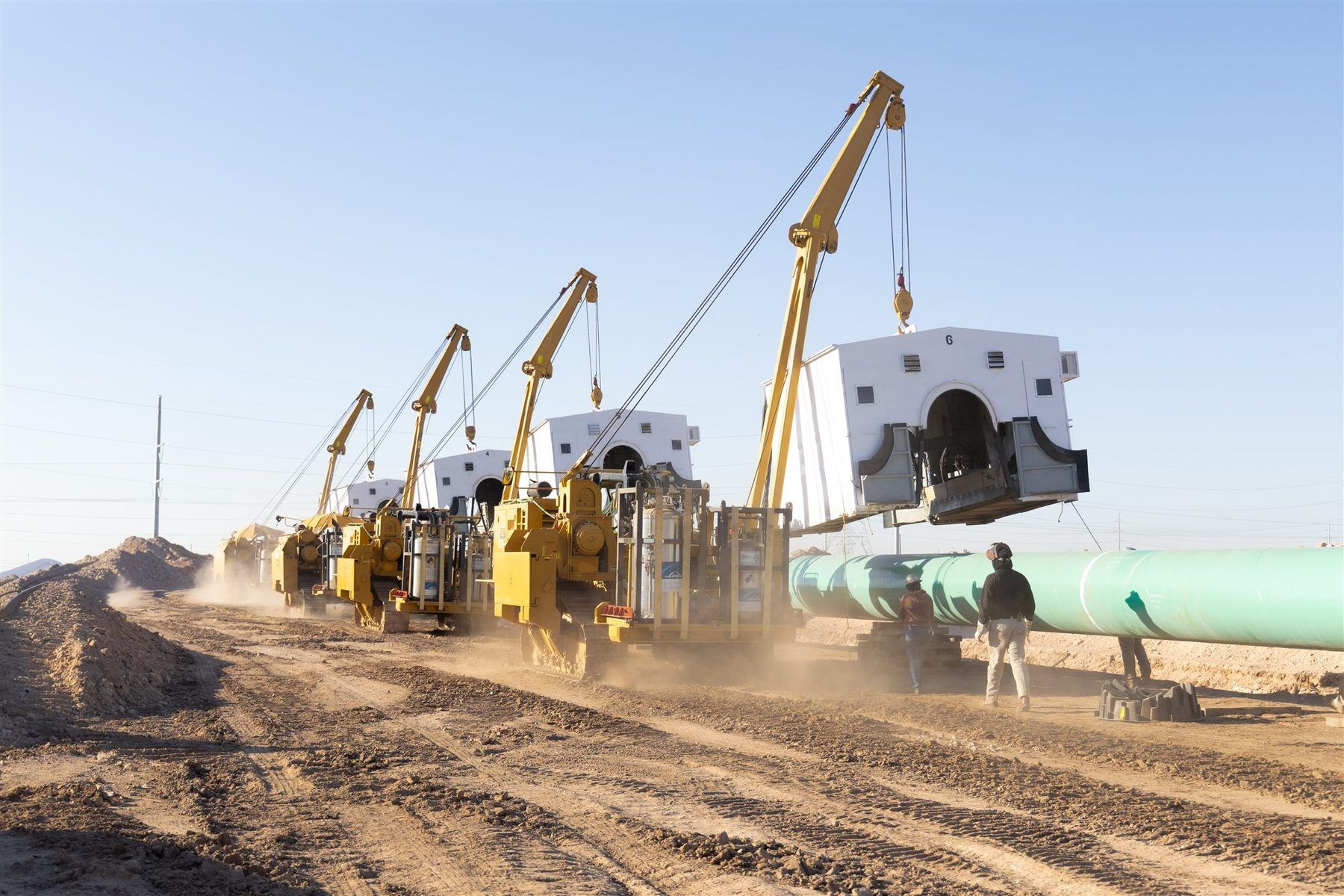 Sidebooms carrying weld shelters along a pipeline firing line on the right-of-way