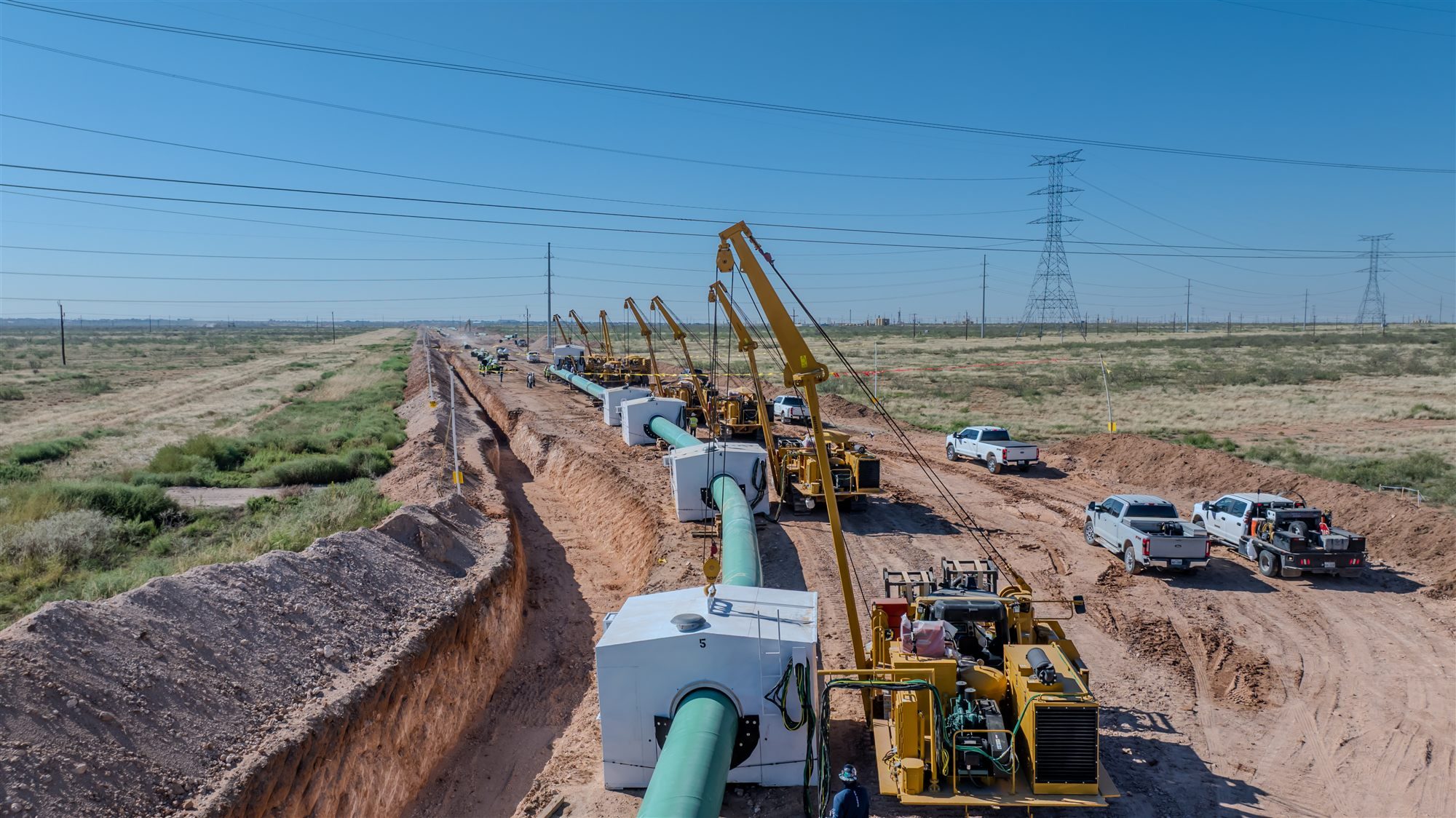 Aerial view of a pipeline construction spread with sidebooms, weld shelters and coated pipe along an open trench