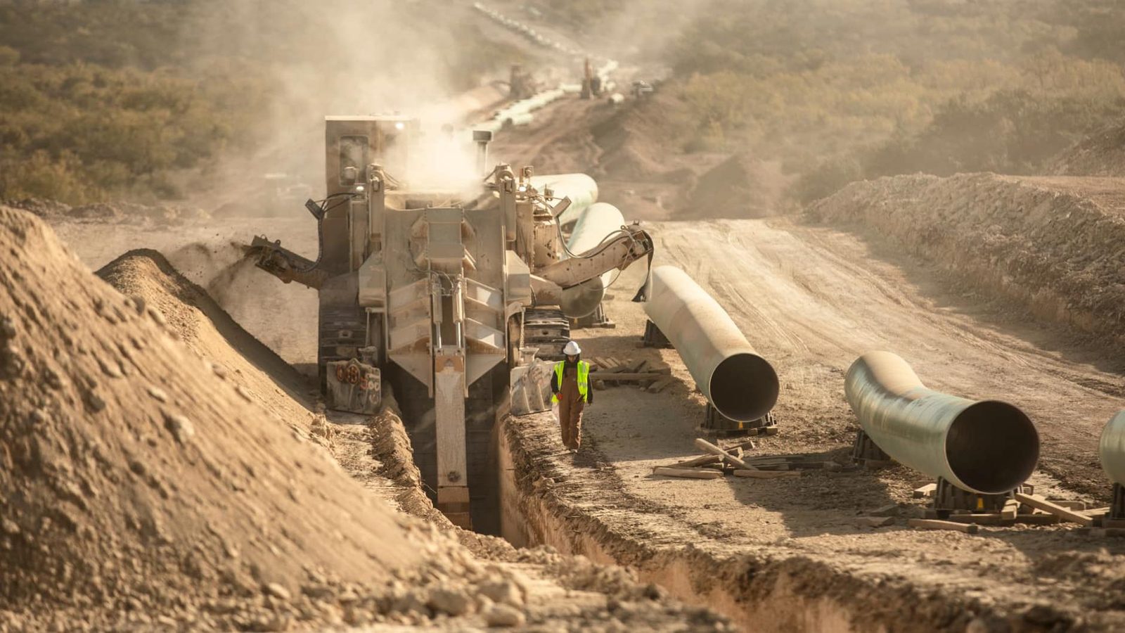 Pipeline trenching and coated pipe staged along a construction spread at golden hour